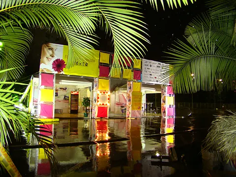 Ambientación nocturna para Éxito con módulos de colores entre palmeras y reflejo en el piso