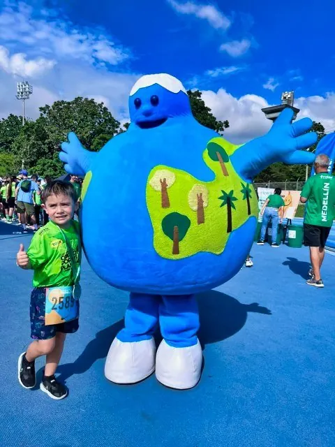 Niño corredor posando con una mascota con forma de planeta Tierra