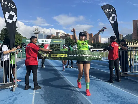 Corredora cruzando la meta de Corro por mi Planeta sobre una pista azul, rodeada de personal del evento