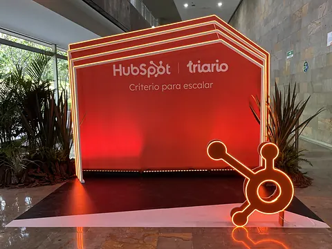 Photo wall de HubSpot y Triario en el Inbound Summit 2026: muro naranja con arcos de neón y la escultura del sprocket de HubSpot