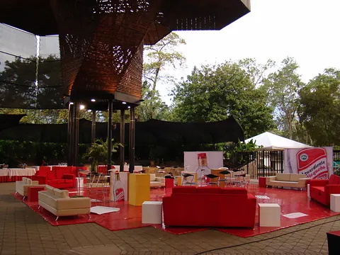 Lounge al aire libre para un evento corporativo, con sofás rojos y blancos junto a una estructura de madera