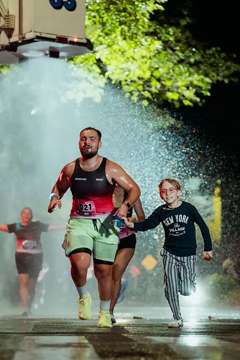 Corredor y un niño de la mano bajo un chorro de agua en la meta nocturna de la Medallo Run