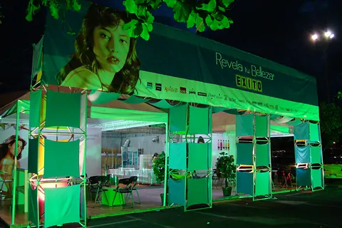 Pabellón iluminado en verde con módulos de exhibición para el evento Revela tu Belleza de Éxito
