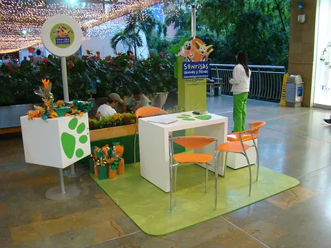 Stand pop-up en un centro comercial, con piso verde, sillas naranjas y señalización de marca