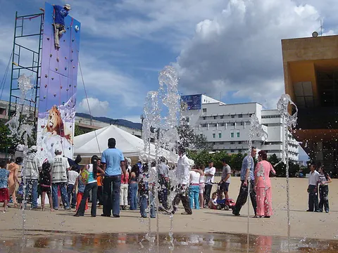 Muro de escalada y fuentes de agua en una plaza llena de gente